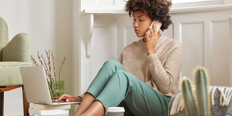 mulher com síndrome de burnout  falando no telefone enquanto mexe no notebook 